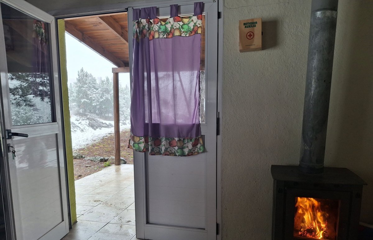 Estufa a leña encendida junto a la puerta de la Cabaña Verde durante la nevada en Villa Yacanto