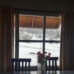 Mesa de la Cabaña Verde frente al ventanal con el paisaje nevado de Villa Yacanto